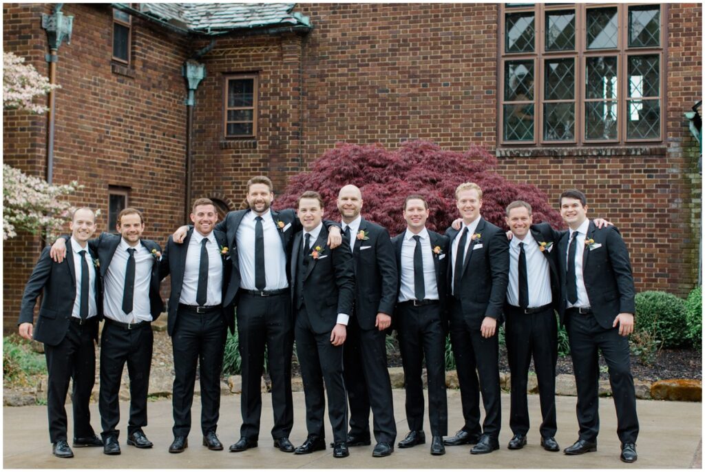 a groom and his groomsmen posing in front of the Tudor house at mason's cove wedding venue