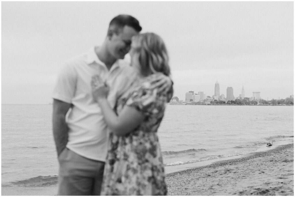 An engaged couple posing at Edgewater park for their engagement session with the cleveland skyline behind them